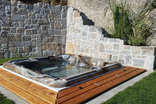 In-ground hot tub installation surrounded by stone masonry walls.